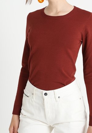 Maglia a maniche lunghe color ruggine con colletto a girocollo, realizzata in tessuto a costine, abbinata a jeans bianchi a vita alta con tasche frontali.