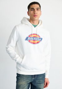 White hoodie with a front pocket, featuring a circular Dickies logo in blue and red. Made from soft fabric with a relaxed fit.