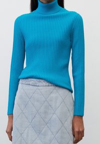 Turquoise geribbelde coltrui van zachte stof. Gecombineerd met een lichtblauwe spijkerrok met een ruitvormig quiltpatroon.