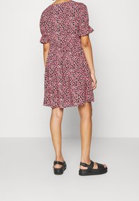 Šaty s květinovým vzorem, krátké volánkové rukávy, růžové a černé barvy. Nosené s robustními černými sandály, po kolena a volného střihu.