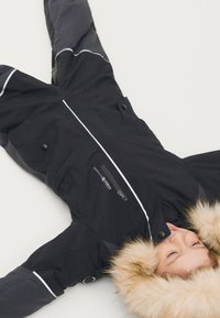 Zwarte geïsoleerde sneeuw overall met een gevoerde capuchon van nepbont, witte accenten, meerdere zakken en een ritszak op de borst.