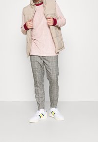 Beige padded vest over a pink long-sleeve shirt with red cuffs, paired with gray plaid pants and white sneakers with green and yellow accents.