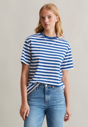 T-shirt rayé avec des lignes horizontales bleues et blanches, col rond, manches courtes et coupe décontractée, associé à un jean en denim taille haute.