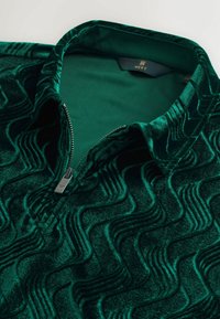 Zielony welurowy pulower z pół zamkiem błyskawicznym, z falistym wzorem tekstury, z suwakiem w kolorze srebrnym i wewnętrzną metką oznaczoną "NEXT."