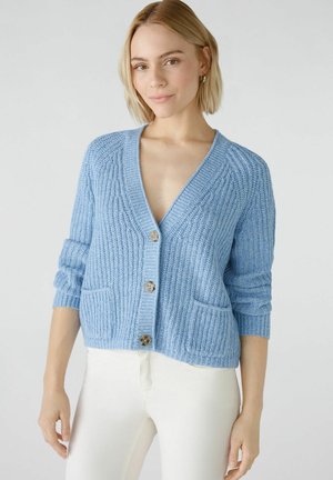 Lichtblauwe cardigan met een diepe V-hals, geribbeld textuur en drie grote knopen. Voorzien van twee voorzakken en opgerolde mouwen.