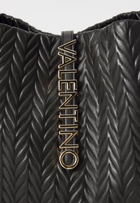 Juodas odinis maišas su akyta, pynimo tekstūra. Apima auksinį "Valentino" logotipą kaip detales ant juodo diržo.