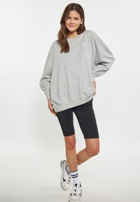 Grå överdimensionerad sweatshirt med sänkta axlar, parat med högmidjade svarta cykelshorts. Vita sneakers med svarta och gröna accenter.