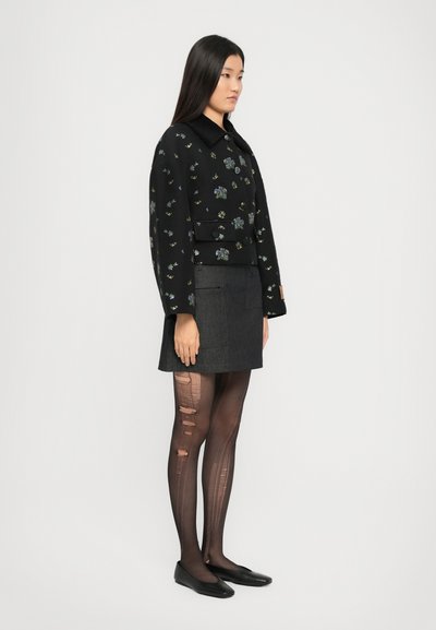 Μαύρο σακάκι με κεντημένα λουλούδια και γιακά, συνδυασμένο με μια σκούρα φούστα και σκιστές μαύρες καλσόν, ολοκληρώνοντας το λουκ με μαύρες μπαλαρίνες.