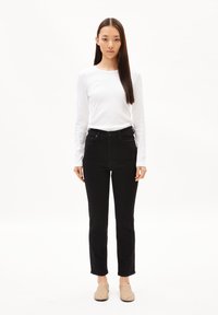 Top de manga larga blanco, jeans negros de cintura alta, zuecos beige. Textura suave, diseño ajustado, corte recto en las piernas y dobladillo vuelto en los jeans.