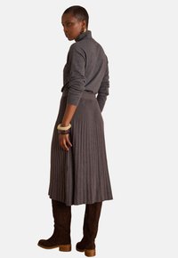 Maglione grigio a coste con collo alto abbinato a una gonna plissettata coordinata, completato da stivali in camoscio marrone e braccialetti texturizzati.