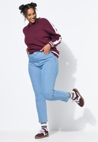 Mörkröd stickad tröja med vita ränder, ljusblå jeans med nitar på sidorna och vinröda sneakers kombinerat med randiga strumpor.