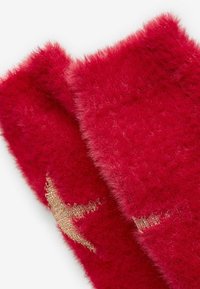 Sciarpa rossa e pelosa con una morbida texture. Presenta un design con filo dorato, che ne enfatizza l'aspetto soffice.