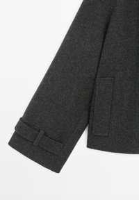 Dark gray wool coat sleeve featuring a cuff with a strap detail and a flap pocket. Material has a textured finish.