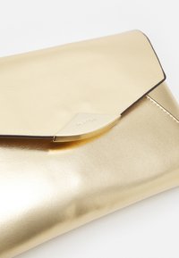 Zlatá metalická psaníčko s elegantním designem obálky, se světlým okrajem a zakřiveným kovovým uzávěrem.
