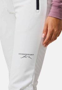 Pantaloni da escursionismo bianchi con vestibilità slim, dotati di una tasca con zip e un logo "SWEDEMOUNT" con una grafica di montagna in ricamo grigio.