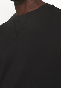 Schwarzer Pullover mit Rundhalsausschnitt und strukturiertem Steppdetail an der Schulter, gefertigt aus einem weichen, glatten Stoff.
