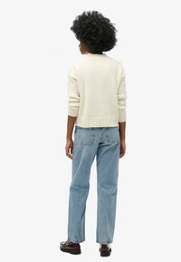 Suéter crema con dobladillo acanalado, utilizado con jeans rectos de color azul claro y zapatos oscuros. Vista desde atrás, mostrando la textura de la tela.