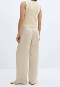 Bezramkowy sweter w jasnym beżu z teksturowanym wzorem, w zestawie z szerokimi spodniami w dopasowanym odcieniu, obie konstrukcje wykonane z lekkiego materiału.