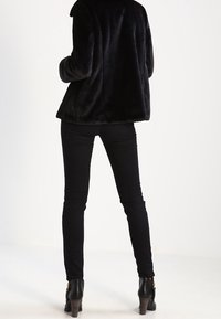 Czarna kurtka z sztucznego futra o luźnym kroju, połączona z dopasowanymi czarnymi dżinsami i botkami na obcasie. Skupienie na fakturze i sylwetce.