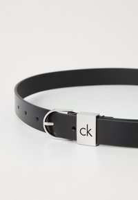 Ceinture en cuir noir avec une texture lisse, dotée d'une boucle en métal argenté avec le logo "ck" et plusieurs trous de réglage.