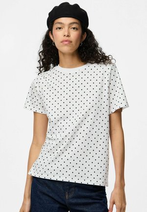 T-shirt blanc à manches courtes avec des pois noirs, col rond et texture de tissu douce. Porté avec un jean en denim noir et un béret noir.