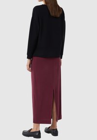 Zwarte sweatshirt met verlaagde schouders, gecombineerd met een bordeaux maxi rok met een zijsplit. Zwarte klompen maken de outfit compleet.