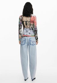 Maglia a maniche lunghe con un design colorato e a fantasia, con un retro trasparente; abbinata a jeans in denim leggero a vita alta di colore blu chiaro con cuciture blu.