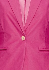 Blazer rose vif avec un seul bouton crème fermé à l'avant et deux poches fentes horizontales de chaque côté.