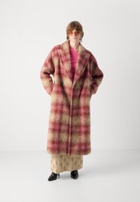 Wollen plaid jas in rode, crèmekleurige en bruine tinten. Heeft een dubbelzijdig ontwerp, grote revers en zijzakken. Combineer met een beige rok en hakken.