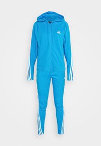 Survêtement Adidas bleu vif avec une veste zippée à capuche et un pantalon assorti avec des bandes blanches sur les manches et les jambes.