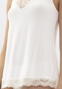 Witte camisole gemaakt van gladde stof, voorzien van een kanten rand langs de onderkant en een kanten detail bij de halslijn in V-vorm.