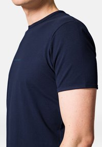 Granatowa koszulka z krótkim rękawem, wykonana z gładkiego, miękkiego materiału. Posiada okrągły dekolt oraz subtelny detal z logo w okolicach klatki piersiowej.