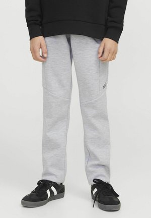 Pantalones de chándal grises con una textura suave, que cuentan con costuras en contraste, paneles laterales y un logo cerca de la cadera derecha. Llevados con zapatillas negras.