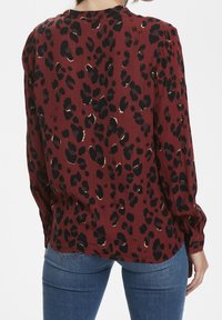 Blusa a maniche lunghe di colore bordeaux con stampa leopardata nera. Tessuto strutturato con polsini abbottonati e orlo curvo.