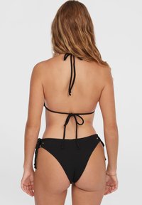 Svart bikini med ett strukturerat halterneck-top som har knytning och lågt skurna bottoms med justerbara sidoknytningar och guldaccenter.