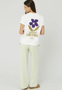 T-shirt blanche avec un motif de fleur violette et le texte "START CREATING" au dos ; associé à un pantalon large à carreaux vert clair.