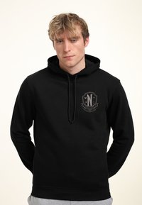 Felpa nera con cappuccio e logo sul petto, con cordino e polsini a coste. Il tessuto appare morbido e liscio, adatto per un abbigliamento casual.