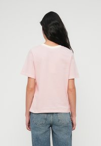 Ρ οζ και λευκό ριγέ κοντομάνικο μπλουζάκι με στρογγυλή λαιμόκοψη και χαλαρή εφαρμογή, σε συνδυασμό με ανοιχτόχρωμο τζιν παντελόνι.