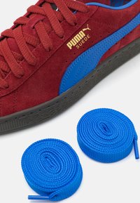 Røde semskede sneakers med sort gummisål og blå detaljer. Inkluderer to blå snørebånd i sneglform, med en tekstureret overflade.