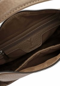 Brūns ādas somas iekšpuse ar rāvējslēdzēja kabatu un mazāku nodalījumu, redzama šuve un daļēji atvērts melns rāvējslēdzējs.