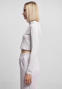 Lys lilla cropped langermet topp med høy krage. Glatt stoff og tettsittende design. Brukt med matchende høyt midjebelte bukser.