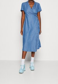 Denim omlottklänning med volangkrage, korta ärmar och medellång längd. Bärs med ljusblå plattformsskor och vita strumpor.