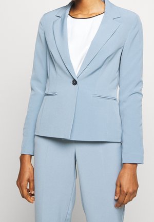 Slim-fit lyseblå blazer med enkelt sort knap over hvid top, parret med matchende lyseblå bukser.
