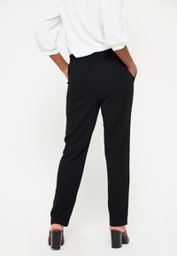 Černé kalhoty s elastickým pasem a zúženým střihem, s bočními kapsami a hladkým povrchem; kombinované s krátkým bílým topem.