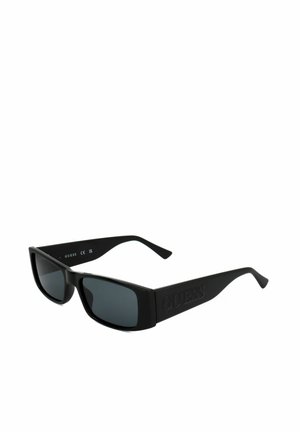Occhiali da sole rettangolari neri Guess con montatura spessa, lenti scure e logo Guess in rilievo sulle aste, posizionati di traverso su sfondo bianco.