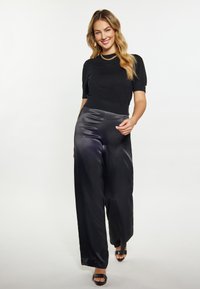 Pulover negru cu mânecă scurtă asociat cu pantaloni din satin cu croială largă în gri închis. Pantofi negri cu vârf deschis. O brățară simplă adaugă detaliu.