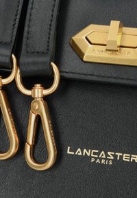 Borsa a tracolla in pelle nera con hardware dorato, inclusi un lucchetto, clip e nome del brand impresso. Texture liscia con design strutturato.