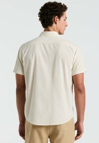 Korte mouw shirt in lichtcrème, met een zachte, gestructureerde stof, bandkraag en een subtiel stiksel aan de achterkant.