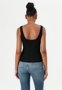 Schwarzes geripptes Tanktop mit runder Rückseite, kombiniert mit hellblauen, eng anliegenden Jeans, die Taschen und eine klassische Denim-Wäsche zeigen.