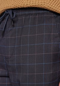 Marinblå rutiga byxor med tyg i blå och rosa rutmönster, dragsko i midjan och sidofickor. Visat i strukturerat material.